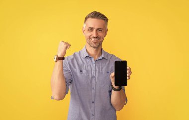 product proposal. advertisement presentation. copy space. happy man presenting phone screen. successful guy showing smartphone on yellow background.