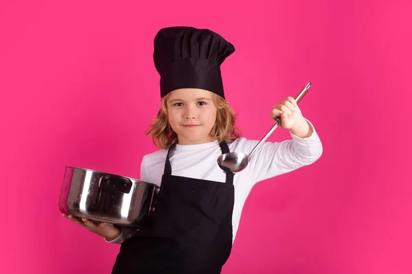 Child chef cook with cooking pot and ladle. Cooking children. Chef kid boy making healthy food. Portrait of little child in chef hat isolated on studio background. Kid chef. Cooking process