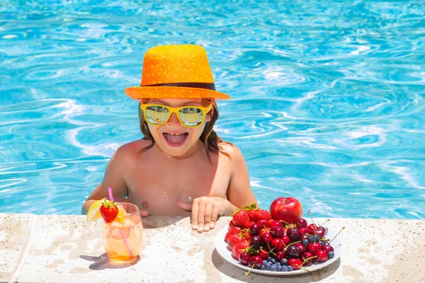 Summer child by the pool eating fruit and drinking lemonade cocktail. Summer kids vacation concept. Little kid boy relaxing in a pool having fun during summer vacation