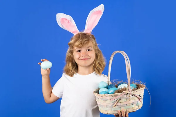 Cute little boy with bunny ears holding easter egg on color blue background. Happy easter holidays. Cute little child wearing bunny ears isolated on blue background