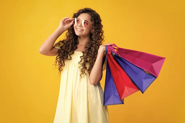Happy teenager portrait. Funny teen girl hold shopping bag enjoying sale isolated on yellow. Portrait of teenager schoolgirl is ready to go shopping. Smiling girl