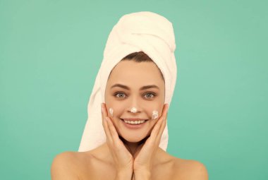 Mutlu genç kadın mavi arka plana yüz kremi sür..