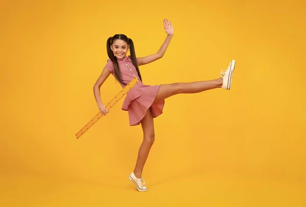 Back to school. School girl hold ruler measuring isolated on yellow background. Crazy jump, jumping kids. Happy teenager, positive and smiling emotions of teen schoolgirl