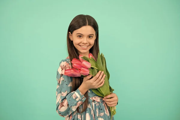 cheerful kid hold flowers for 8 of march. teen girl with spring bouquet on blue background. floral present. child with tulips. mothers or womens day.