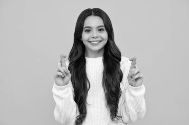 Happy face, positive and smiling emotions of teenager girl. Joyful teenager girl fingers crossed, makes desirable wish, waits for good news. Lucky child keeps fingers crossed, believes in good luck