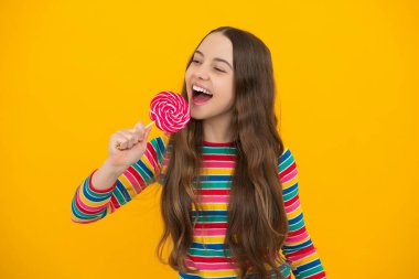 Teen girl hold lollipop caramel on yellow background, candy shop. Teenager with sweets suckers. Excited face, cheerful emotions of teenager girl