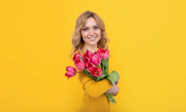 smiling young woman with spring tulip flowers on yellow background.