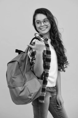 Okul üniformalı okul çantalı kız. Okul çocuğu, genç öğrenci sırt çantasını sarı izole edilmiş arka planda tutuyor. Mutlu ergen, pozitif ve gülümseyen genç kız duyguları