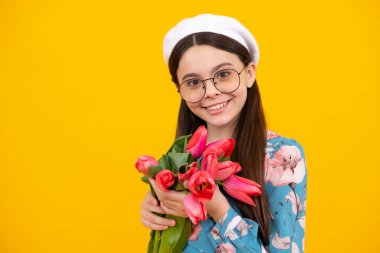 Beautiful smiling trendy teen girl with bouquet of tulips on yellow studio background. Girl enjoying flowers