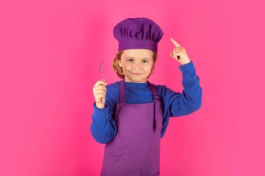 Funny kid chef cook with spoon. Kid in cooker uniform and chef hat preparing food on studio color background. Cooking, culinary and kids food concept