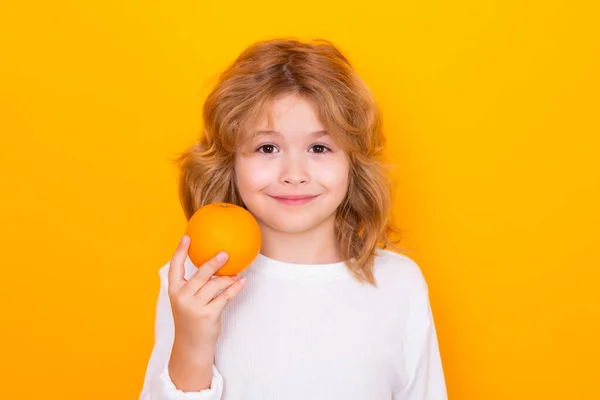 Kid with orange in studio. Studio portrait of cute child hold orange isolated on yellow background