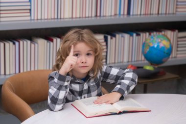 Education, knowledge and bookstore concept. Child reading a red book in the library. Little student on school library
