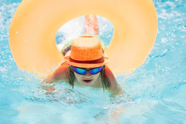 Child in swimming pool on inflatable ring. Kid swim with orange float. Water toy, healthy outdoor sport activity for children. Kids beach fun. Fashion summer kids