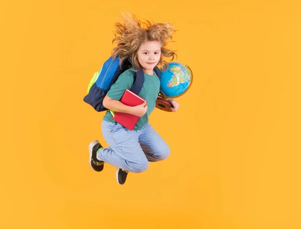 Kid jump and enjoy school. Funny excited school concept. Little student boy with backpack go to study, jumping. Schoolchild, pupil jump on yellow isolated background