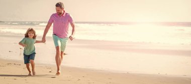 Baba ve oğulun bayrağı yaz deniz sahillerinde koşuyor. Mutlu baba ve çocuk aileleri plajda koşuşturuyor..