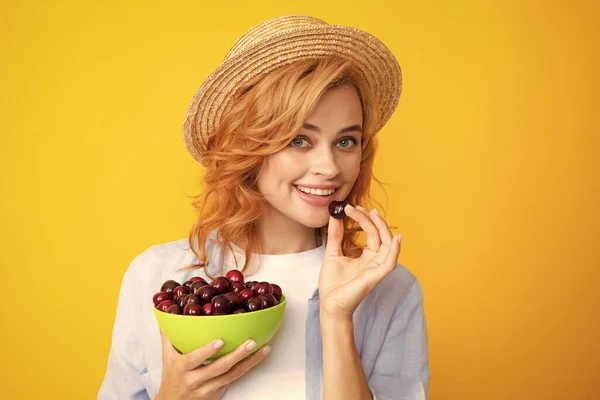 Picking eating cherry fruit. Attractive young woman eating fresh cherry. Healthy summer fruits. Yellow background. Beautiful woman posing with a cherry, girl with cherry promoting