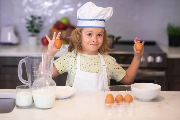 Kid chef cook with eggs at kitchen. Funny kid chef cook cookery at kitchen. Chef kid boy making healthy food. Portrait of little child in chef hat