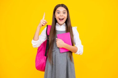 Excited face. Back to school. Schoolgirl student hold book on yellow isolated studio background. School and education concept. Teenager girl in school uniform. Amazed expression, cheerful and glad