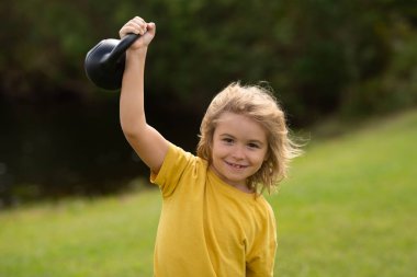 Kid lifting the kettlebell in park outside. Sport child workout. Child exercising with kettlebell. Sporty child with dumbbell. Fit kids training