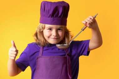 Funny kid chef cook with kitchen ladle, studio portrait. Excited chef cook. Child wearing cooker uniform and chef hat preparing food, studio portrait