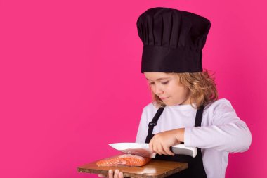 Child cook hold cutting board with fish salmon steak and knife. Child chef cook, studio portrait. Kids cooking. Teen boy with apron and chef hat