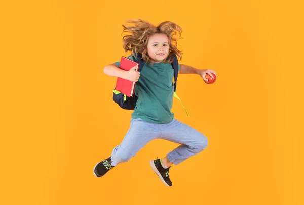 Kid jump and enjoy school. Funny child school boy jumping on a yellow studio background