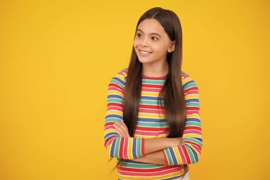 Teenage girl kid with crossed arms, looking at camera, isolated on yellow studio background. Happy face, positive and smiling emotions of teenager girl
