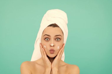 Şaşırmış genç kız mavi arka plana yüz kremi sür..