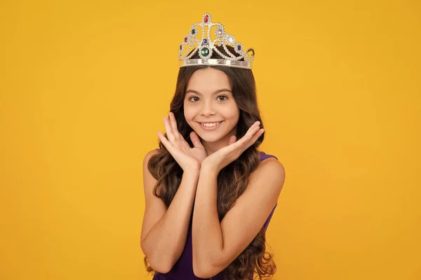 Little queen wearing golden crown. Teenage girl princess holding crown tiara. Prom party, childhood concept. Happy girl face, positive and smiling emotions