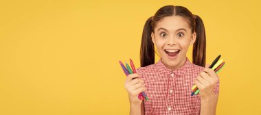 Hayretler içindeki genç kızlar resim yapmak için renkli kalemler bulundururlar. Yaratıcı bir zihin. Öğrenci portresi, stüdyo afişi. Okul çocuğu yüzü, boşluklar