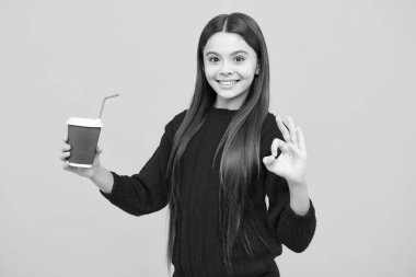 Sarı stüdyo arka planında kahve ya da çay fincanı olan çocuk. İçki ısmarlayan ergen kız.