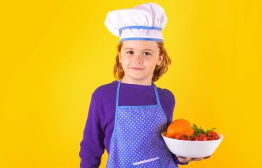 Kid cook hold plate with vegetables. Child chef cook, studio portrait. Kids cooking. Teen boy with apron and chef hat