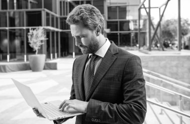 İş adamı gibi giyinmiş ciddi bir girişimci ofis dışında bilgisayar kullanıyor, serbest çalışıyor..