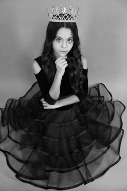 Balo elbiseli genç bencil kız başarıyı kutluyor. Kraliçe tacındaki genç çocuk gri arka planda izole edilmiş. Tacın içindeki prenses kız. Balo partisi.