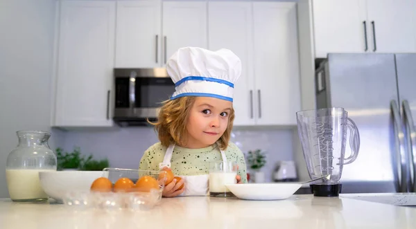 Children cooking in the kitchen. Funny kid chef cook cookery at kitchen. Chef kid boy making healthy food. Portrait of little child in chef hat