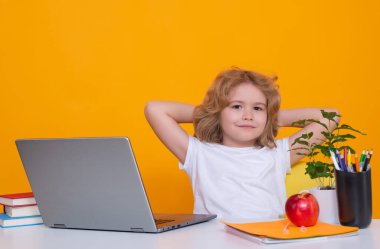 School child using laptop computer. Kid boy from elementary school with book on yellow isolated background. Little student, smart nerd pupil ready to study. Concept of education and learning