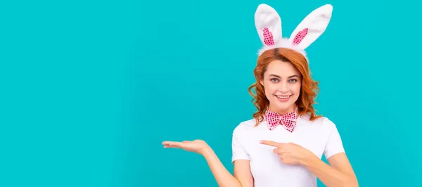 Easter bunny girl. Woman isolated face portrait, banner with mock up copyspace. happy easter woman in bunny ears and bow tie presenting product and point finger on blue background