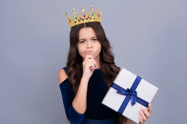 Teenager child princess in crown with gift box. Present for holidays. Happy birthday, Valentines day, New Year or Christmas. Kid hold present box with gift ribbon bow. Angry face, upset emotions of