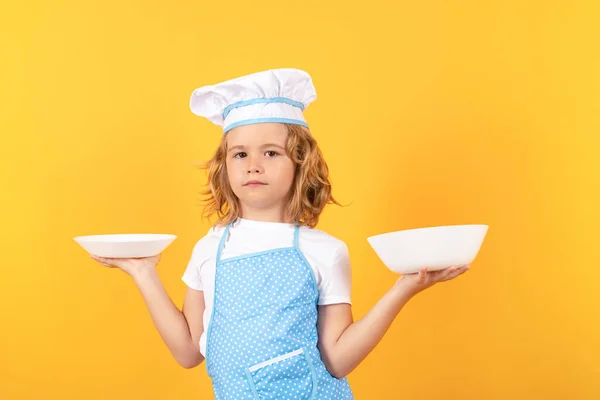 Funny kid chef cook with kitchen plate, studio portrait. Kid chef cook prepares food on isolated studio background. Kids cooking. Teen boy with apron and chef hat preparing a healthy meal