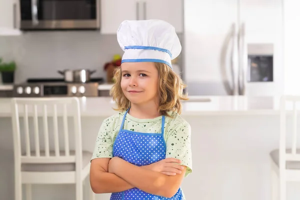 Portrait of funny child chef in kitchen. Children cooking in the kitchen. Funny kid chef cook cookery at kitchen. Chef kid boy making healthy food. Portrait of little child in chef hat
