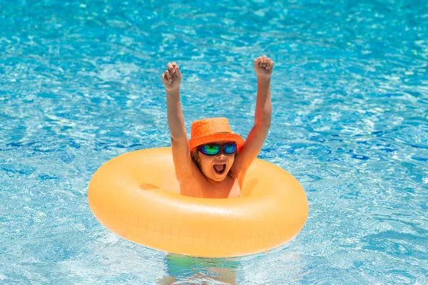 Child with inflatable ring in swimming pool. Kid boy swim in outdoor pool of tropical resort. Hot Summer. Water toys and floats for kids