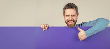 İnsan yüzü portresi, fotokopi alanı olan pankart. ürün sunumu. Yenilik bilgisi sunuyorum. Mavi kağıdın arkasındaki erkek baş parmağını gösteriyor.