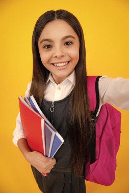 Okul çantalı genç kız sarı izole edilmiş stüdyo geçmişi üzerine kitap tutuyor. Çocuk okulu ve eğitim konsepti