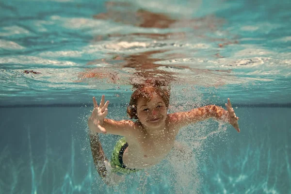 Underwater child in the swimming pool. Cute kid boy swimming in pool under water