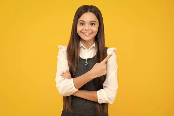 Look at advert. Teenager child points aside shows blank copy space for text promo idea presentation, poses against yellow background. Happy girl face, positive and smiling emotions