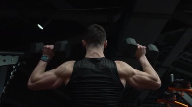 Fit adam spor salonunda dambılları kafasının üzerinden kaldırıyor. Triseps kollu bir sporcu spor salonunda dambıl üstünde egzersiz yapıyor. Fiziksel zindelik. Spor ve zindelik.