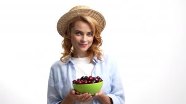 cheerful lady farmer in straw summer hat taking cherry from bowl to eat, healthy food.