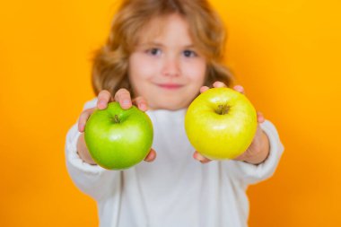 Close up kid with apple in studio, selective focus. Studio portrait of cute child hold apple isolated on yellow background