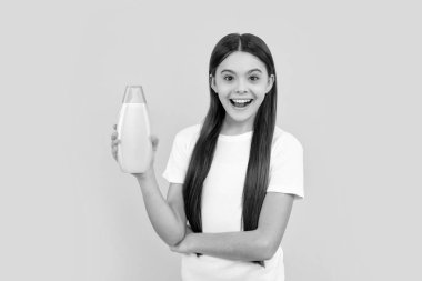 Şaşkın çocuk sarı arka planda saç kremi şişesini tutuyor, güzellik.