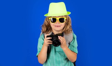 Stüdyo arka planında kamera ve sırt çantalı çocuk gezgin. Turist çocuk. Seyahat çantasıyla çocuk portresi. Seyahat, macera, tatil